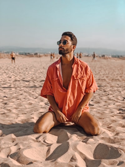 During the day, a man wearing orange button shirt sitting on the beach
